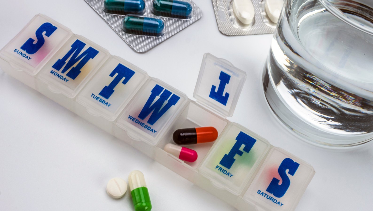 A weekly pill organizer with medications on a table
